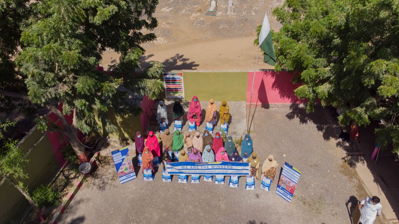 Aerial drone shot of women gathered in colorful dress at school courtyard with WANG banners
