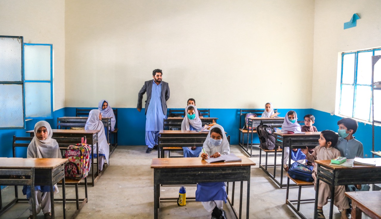 Girls at desks in rural Balochistan school classroom with teacher