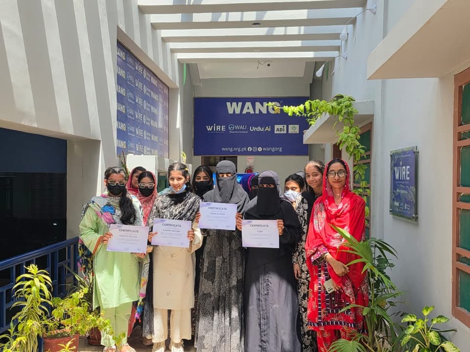Young women graduates holding certificates outside the WANG Lab of Innovation