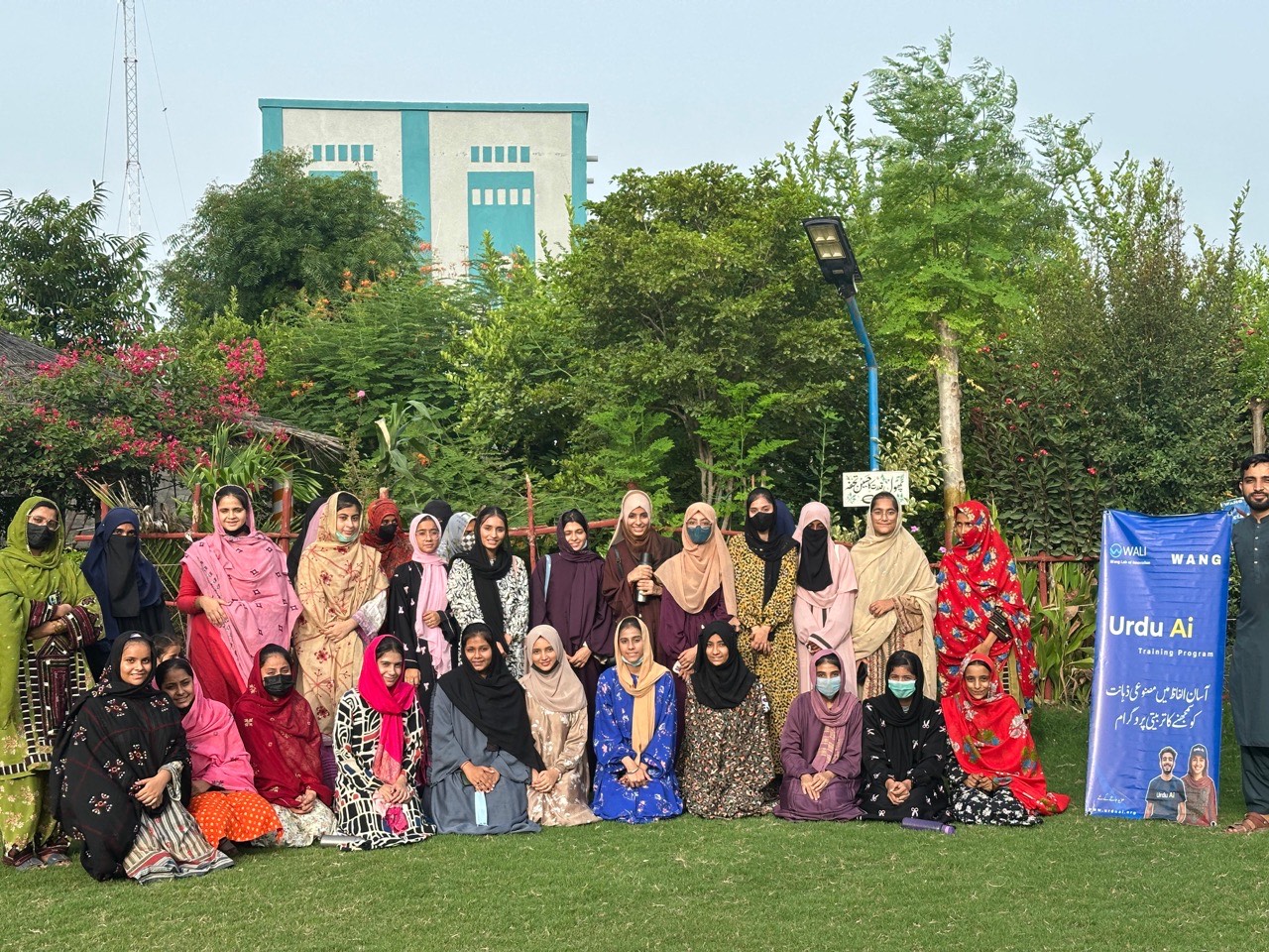 Over 30 women in colorful dress at Urdu AI training group photo with WANG banner in Pakistan